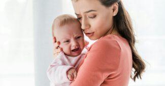 attractive mother holding in arms crying infant at home