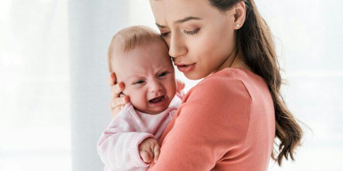 attractive mother holding in arms crying infant at home